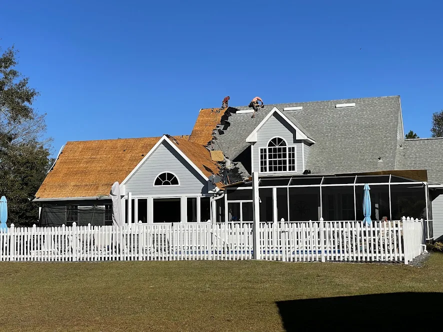 Wide shot of a two-story home mid tear-off with the crew on the ridge.
