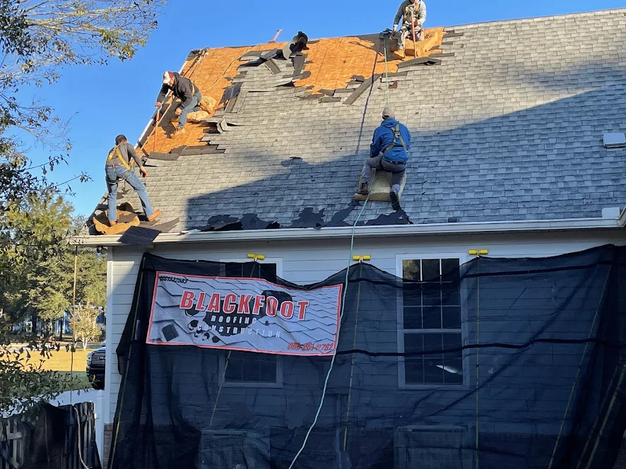 Blackfoot Roofing crew mid tear-off with the branded jobsite banner hung on the home.